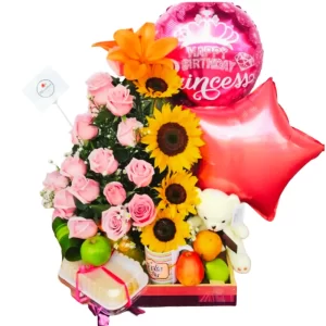 Arreglo floral desayuno sorpresa con rosas rosadas, girasoles, globo de "Happy Birthday Princess", globo de estrella, oso de peluche, frutas frescas (manzana, naranja) y porción de pastel, ideal para cumpleaños.